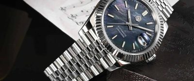 San Martin SN0058 Retro Homage Dress Watch featuring a stainless steel case and bracelet with a fluted bezel. The watch has a black mother-of-pearl dial with silver hour markers and hands, a date window with a magnifier, and is automatic with 100m water resistance. Displayed in a close-up, showcasing its luxurious and refined design.