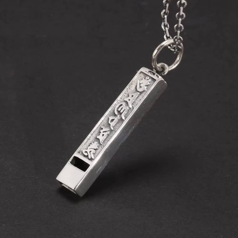 Close-up of engraved silver whistle-shaped pendant with Tibetan mantra