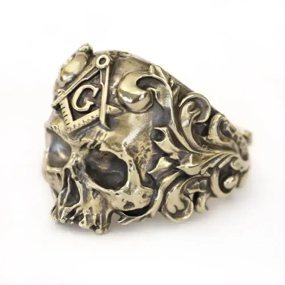 Metal skull ring featuring intricate engravings and a raised Masonic square and compass insignia.