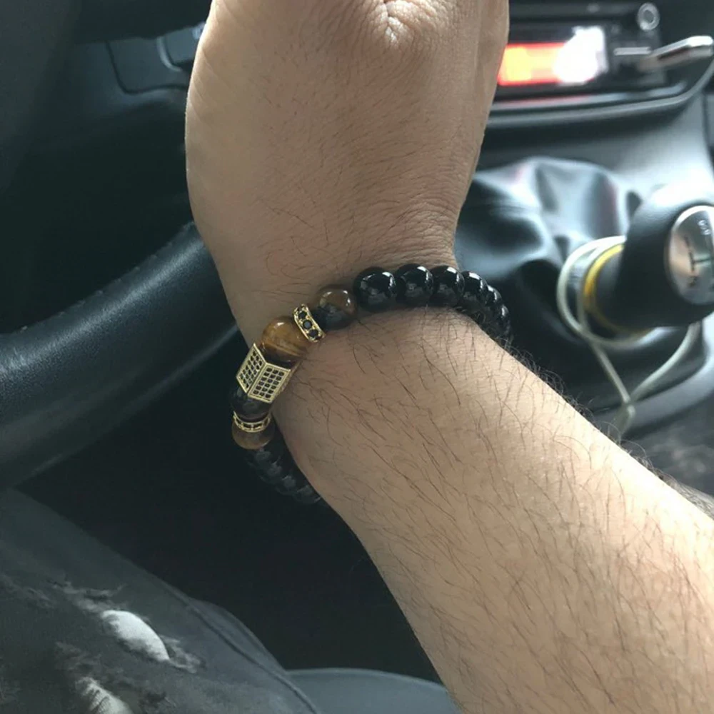 Close-up of a trendy black and gold beaded bracelet worn by a man inside a car, showcasing masculine jewelry style.
