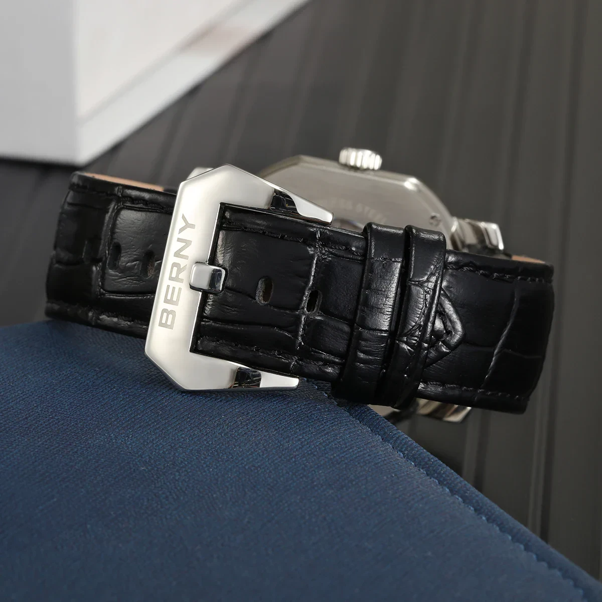 Detailed image of a stylish black leather watch strap featuring a silver buckle engraved with 