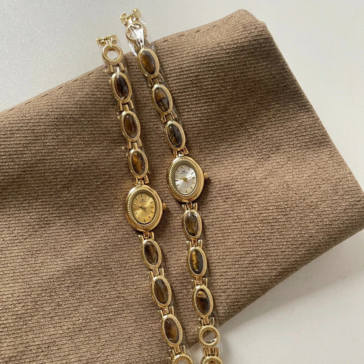 Gold oval watch with gemstone accents on jewelry chain, luxury women’s wristwatch style.