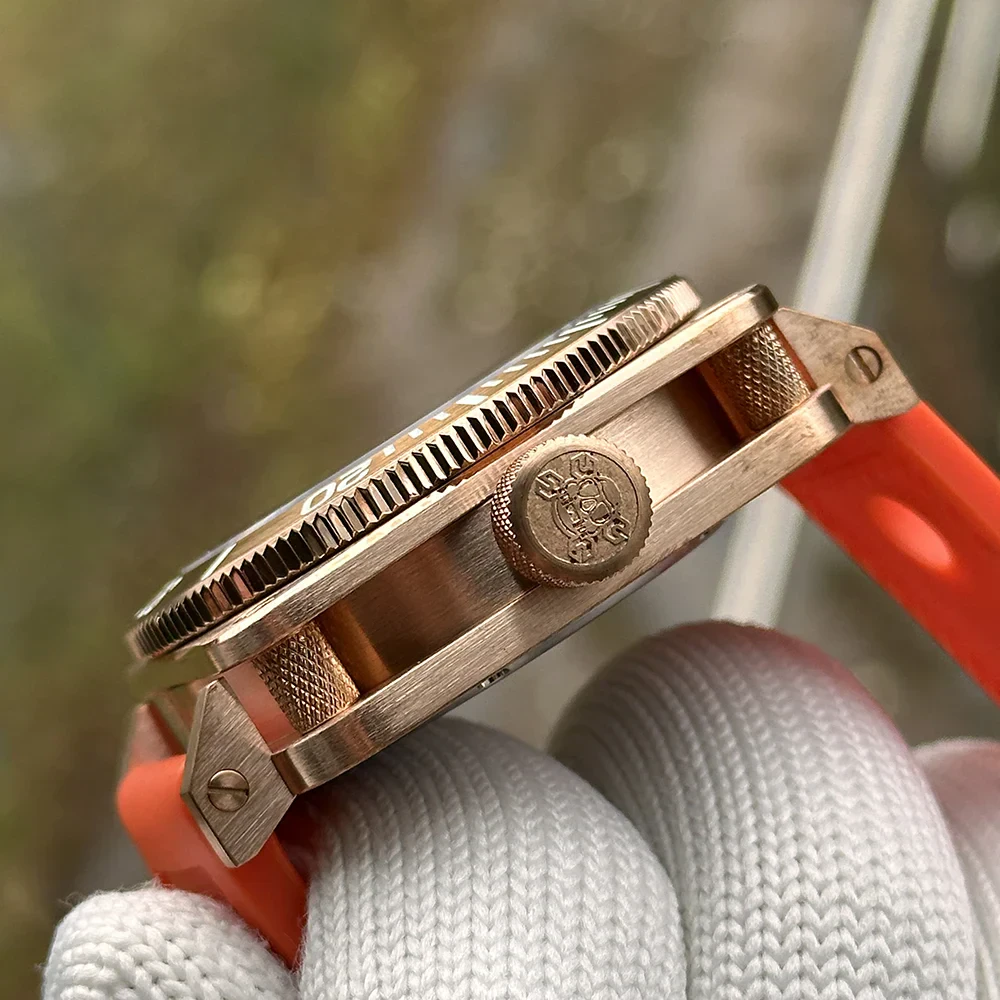 Close-up of a bronze-cased dive watch with orange rubber strap and black dial.