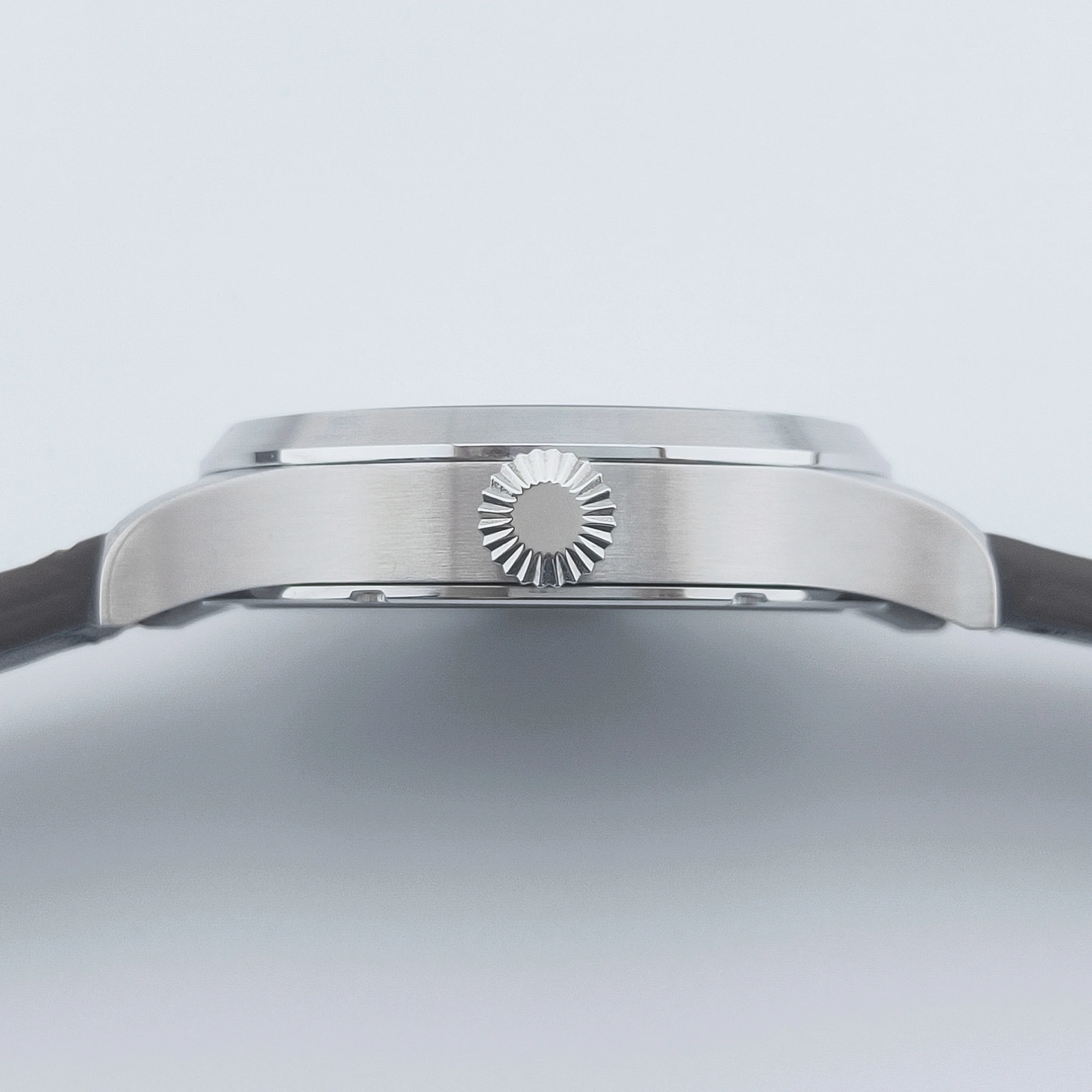 Close-up of stainless steel watch crown with black leather strap.