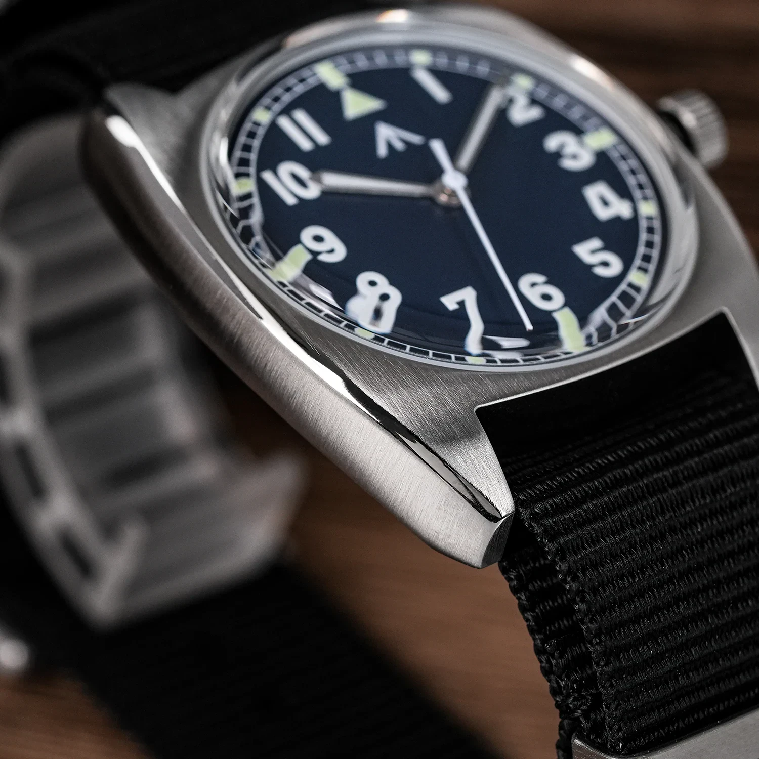 Vintage military wristwatch with black dial, luminous hands, and black fabric strap.