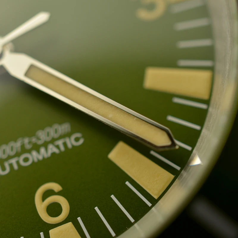 Green watch dial with luminous hour and minute hands, detailed minute markers, and a sleek design.